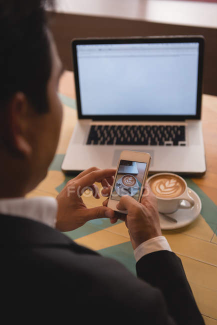 Businessman clicking photo of coffee in coffee shop — Stock Photo