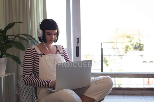 Молода жінка з навушниками, використовуючи ноутбук вдома — стокове фото
