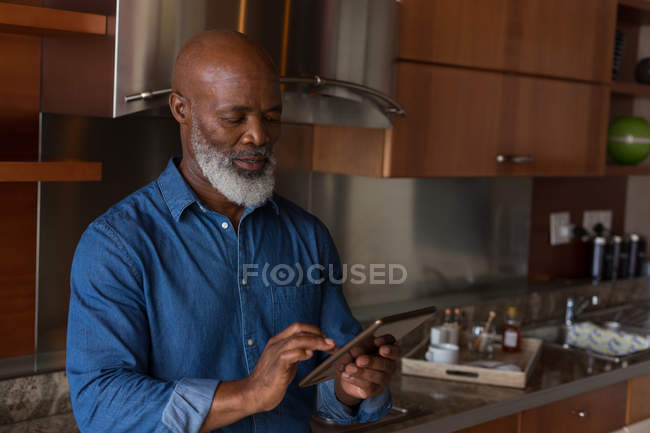 Homem sênior usando tablet digital na cozinha em casa — Fotografia de Stock