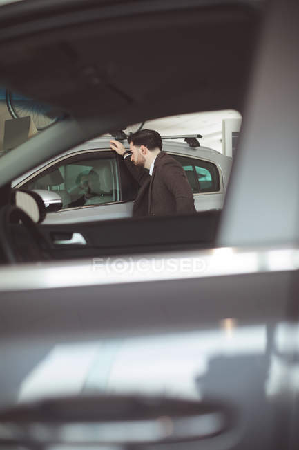 Beau vendeur examinant voiture au showroom — Photo de stock