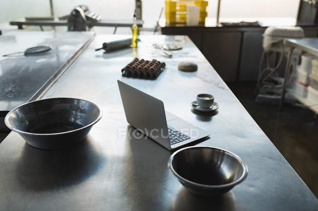 Ordenador portátil, café y utensilios en una mesa en la panadería - foto de stock