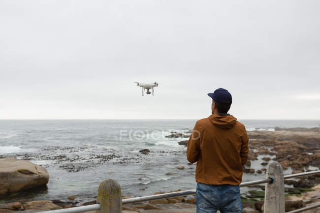Rear view of man operating a flying drone near beach — Stock Photo