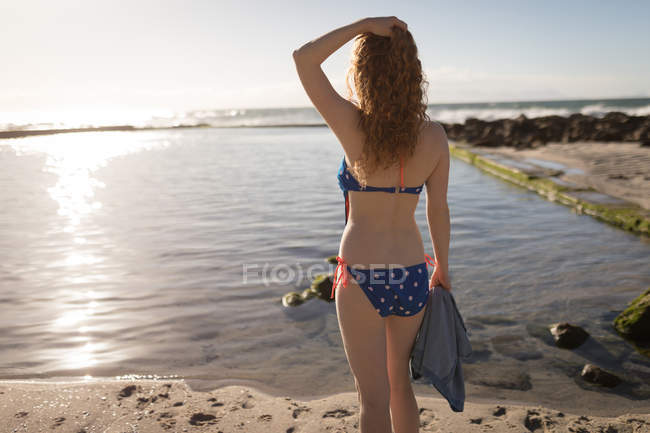 Вид сзади на привлекательную женщину в бикини, стоящую у берега моря — стоковое фото