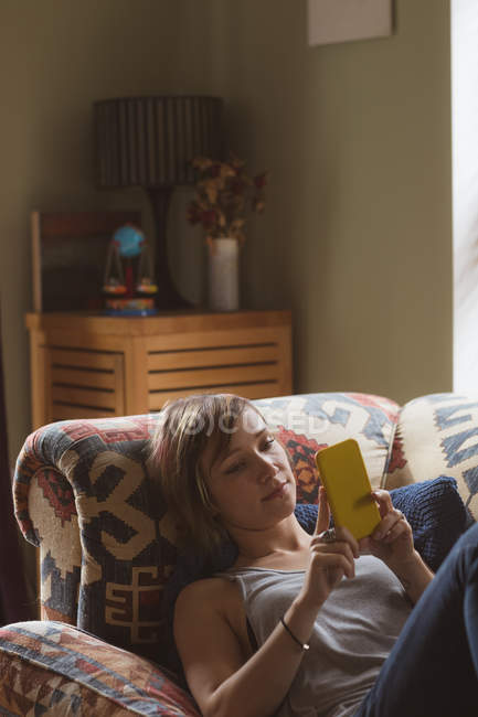 Frau benutzt Handy, während sie auf Sofa im Wohnzimmer liegt — Stockfoto