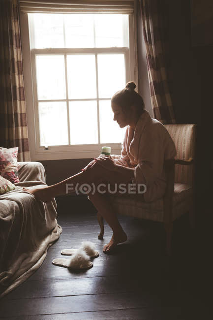 Mujer joven aplicando loción corporal en casa - foto de stock