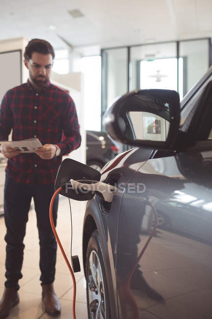 Salesman standing next to car and reading brochure outside the showroom — Stock Photo