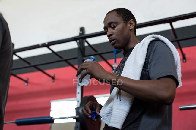 Человек пьет воду из бутылки воды в тренажерном зале — стоковое фото
