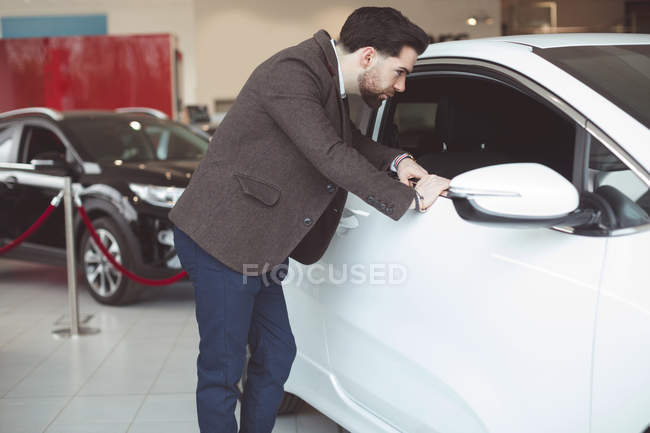 Beau vendeur examinant voiture au showroom — Photo de stock