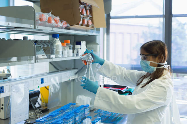 Scientifique versant une solution chimique sur une fiole conique d'une bouteille en laboratoire — Photo de stock