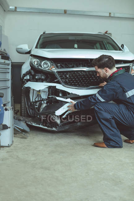 Mecánico examinar coche dañado en el garaje de reparación - foto de stock