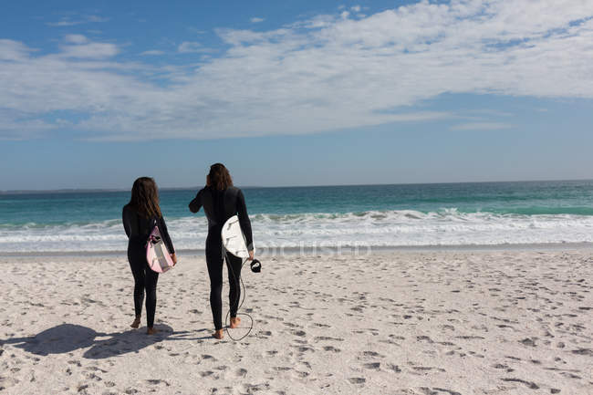 Вид сзади на пару серферов, идущих с доской для серфинга на пляже — стоковое фото