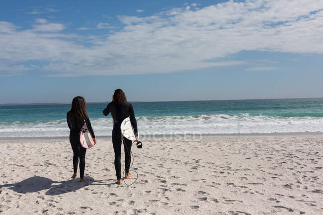 Rear view of surfer couple walking with surfboard in the beach — Stock Photo