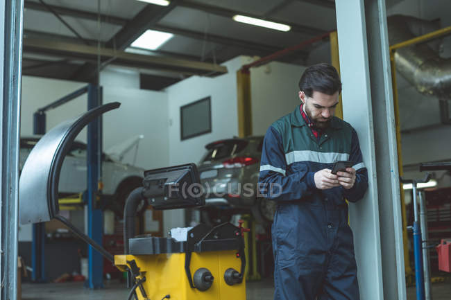 Mecânico usando telefone celular na garagem de reparação — Fotografia de Stock