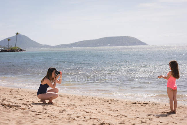 Mãe fotografando sua filha com câmera digital na praia — Fotografia de Stock