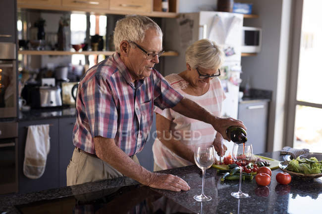Senior man pouring wine into wine glass at home — Stock Photo