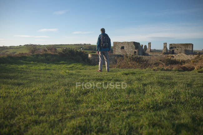 Вид сзади мужчины-туриста, стоящего с рюкзаком в сельской местности — стоковое фото