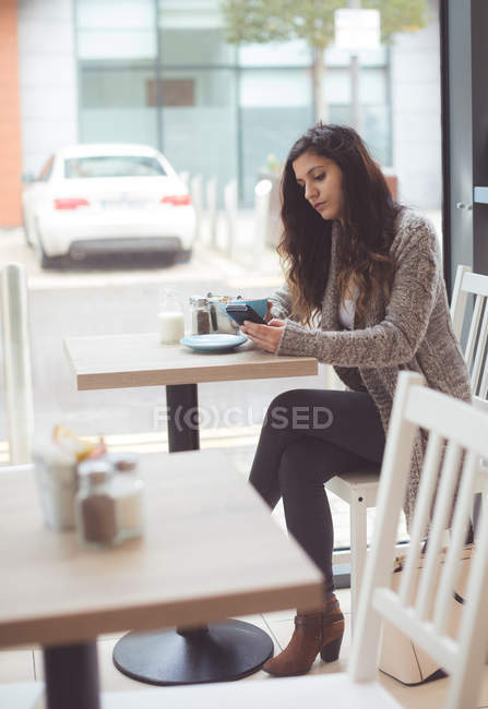 Жінка використовує мобільний телефон, маючи каву в кав'ярні — стокове фото