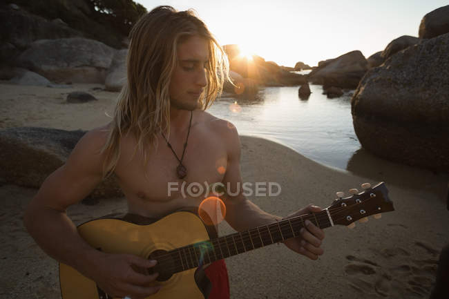 Homem tocando guitarra na praia ao entardecer — Fotografia de Stock