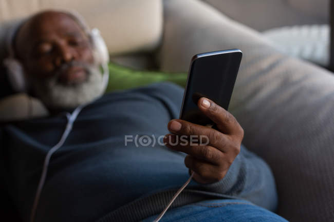 Homme âgé écoutant de la musique sur smartphone à la maison — Photo de stock