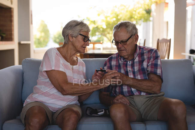 Старшая пара проверяет сахар в крови с помощью глюкометра дома — стоковое фото