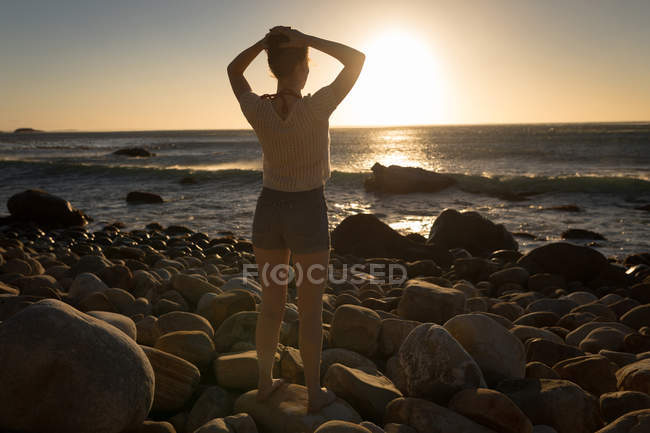 Vue arrière de la femme debout sur le rocher au coucher du soleil — Photo de stock