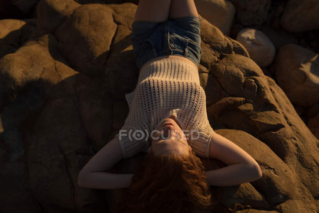 Donna che si rilassa sulla roccia in spiaggia durante il tramonto — Foto stock