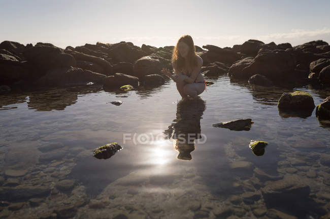 Woman crouching in shallow water on a sunny day — Stock Photo