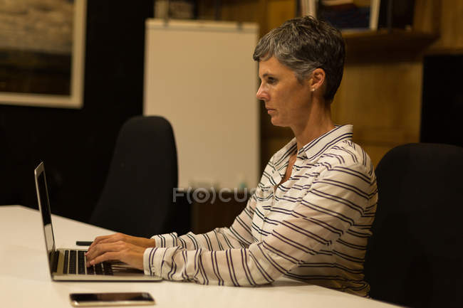 Madura mujer de negocios utilizando el ordenador portátil en el escritorio en la oficina - foto de stock
