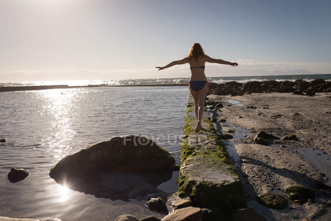 Mulher andando borda da piscina à beira-mar em um dia ensolarado — Fotografia de Stock