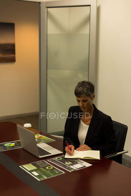 Mature businesswoman writing in diary at office desk — Stock Photo