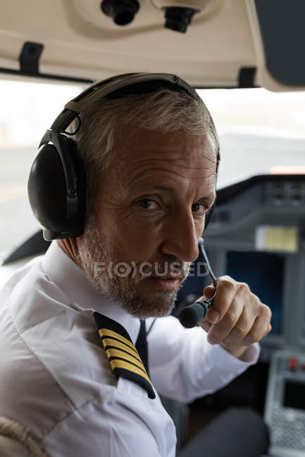 Retrato do piloto masculino falando no fone de ouvido no cockpit — Fotografia de Stock