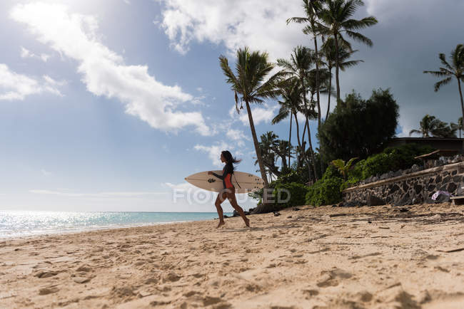 Frau läuft an einem sonnigen Tag mit Surfbrett am Strand — Stockfoto