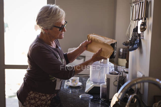 Donna anziana che mette il latte in caffettiera in cucina — Foto stock