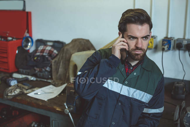 Mecânico falando no telefone celular na garagem de reparação — Fotografia de Stock