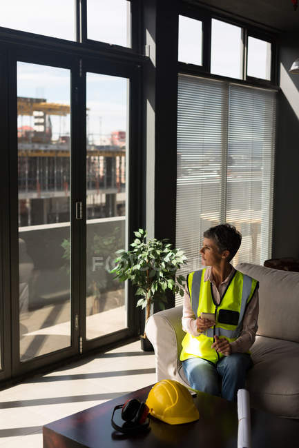 Female architect with mobile phone looking through window in the office — Stock Photo