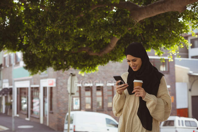 Усміхнений хіджаб жінка переглядає фотографії на мобільному телефоні на вулиці — стокове фото