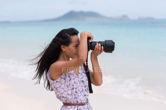 Молодая женщина щелкает фото с цифровой камерой на пляже — стоковое фото