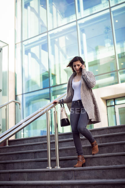 Young woman talking on mobile phone while walking downstairs in the city — Stock Photo