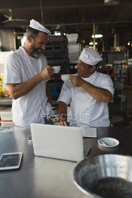 Hombre panadero tomando café con su compañero de trabajo en la panadería - foto de stock