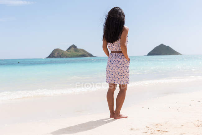 Frau steht an einem sonnigen Tag mit den Händen in der Tasche am Strand — Stockfoto
