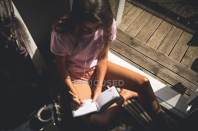 Mulher escrevendo em um diário na sala de estar em casa — Fotografia de Stock