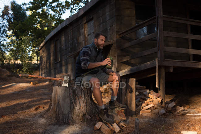 Hombre reflexivo con botella de agua sentado en el tocón del árbol - foto de stock