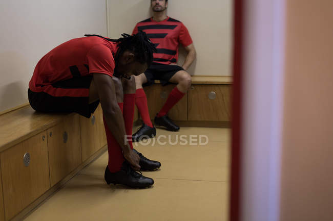 Vista lateral del jugador de fútbol atando su zapato de encaje en el vestidor - foto de stock