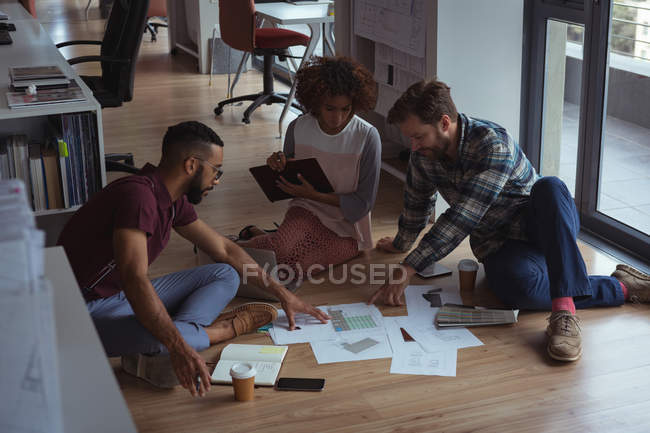 Architects discussing over document on floor in the office — Stock Photo