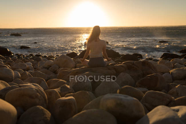 Вид ззаду жінка робить медитацію на скелі на заході сонця — стокове фото