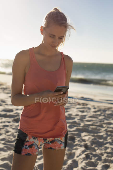 Jogadora de voleibol feminina usando telefone celular na praia — Fotografia de Stock