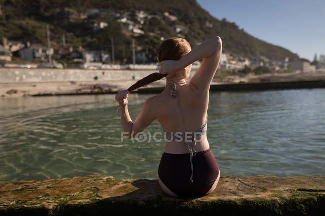 Vista trasera de la mujer mojando su cabello cerca de la piscina junto a la playa - foto de stock