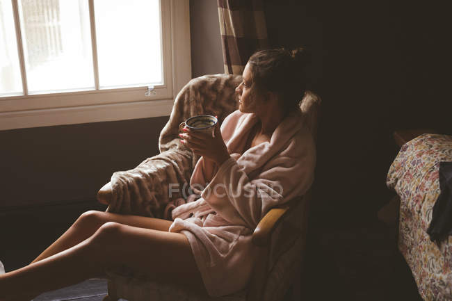 Femme réfléchie prenant un café dans le salon à la maison — Photo de stock
