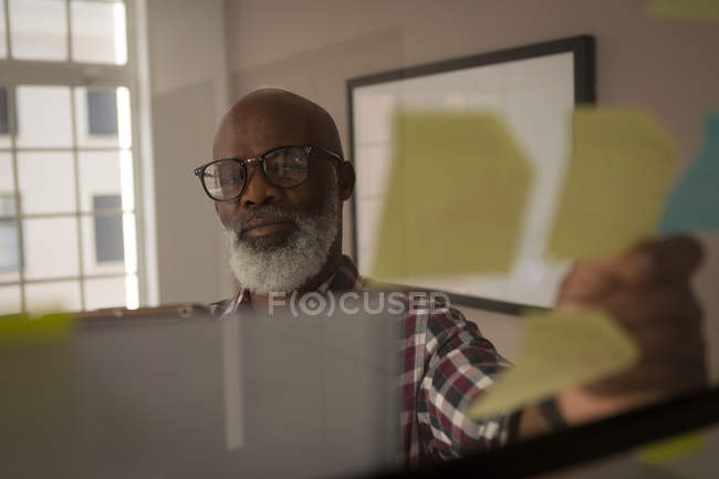 Senior graphic designer looking at sticky notes in office — Stock Photo
