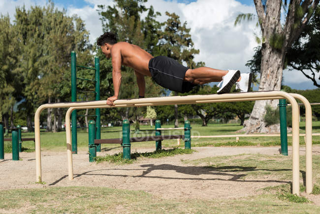 Hombre haciendo ejercicio en barra paralela en el parque en un día soleado - foto de stock